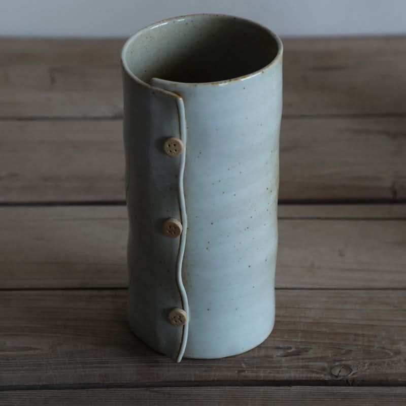 Grey textile-folded ceramic cup with wooden buttons on a rustic wooden surface.